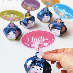 May include: A set of colorful Kokeshi paper doll favor boxes with different messages on the umbrellas. The messages include "I Love You", "Happy Birthday", "For Robin", and "Make a Wish".