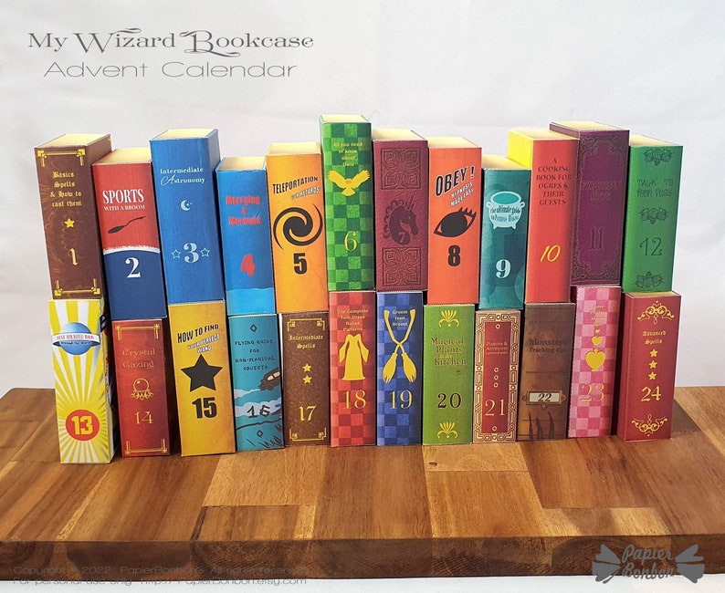 May include: A wizard-themed advent calendar with 24 miniature book-shaped boxes, each with a different title and number. The boxes are arranged in a bookcase shape on a wooden surface. The calendar is titled "My Wizard Bookcase Advent Calendar".