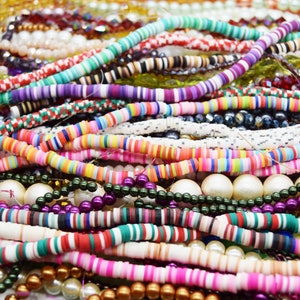 May include: A close-up of a selection of colourful beaded necklaces and bracelets. The beads are made from a variety of materials, including plastic, wood and glass. The necklaces and bracelets are arranged in a random pattern, creating a visually appealing and textured display.