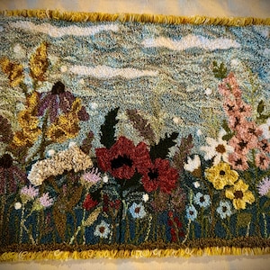 May include: A rug depicting a field of flowers with a blue sky background. The flowers are red, yellow, pink, and purple. The rug has a fringed border.