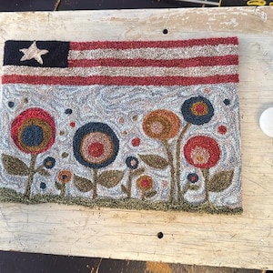 May include: A hand-stitched rug depicting a stylized American flag with red and white stripes and a blue field with a white star. Below the flag is a design of colorful flowers with green stems and leaves.