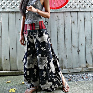 May include: A woman wearing a grey tank top and black pants with a white and black fish print. She is holding a red and white Japanese umbrella.