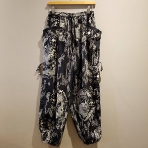May include: Black pants with a white dragon and cloud pattern. The pants have a drawstring waist and side pockets.