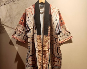Pode incluir: Robe estilo quimono estampado com gola e acabamentos pretos, pendurado num cabide de madeira. O robe apresenta um fundo bege com desenhos abstratos castanhos, pretos e vermelhos. As mangas são curtas e o robe é aberto na frente.