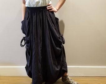 Puede incluir: Una falda maxi negra con un diseño fruncido y una cintura con cordón. La falda tiene dos bolsillos a los lados y una cremallera en la parte delantera.