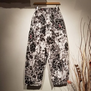 May include: White pants with a black floral print. The pants have a wide leg and a drawstring waist.