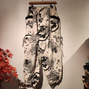 May include: White pants with a black and white print of koi fish. The pants have a drawstring waist and a loose fit.