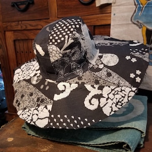 May include: A black and white patterned sun hat with a wide brim. The hat is made of fabric and has a patchwork design.