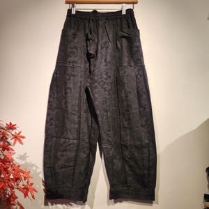 May include: Black patterned pants with a drawstring waist and pockets. The pants are made of a dark fabric with a subtle, repeating design. The loose fit and comfortable style make them suitable for casual wear.