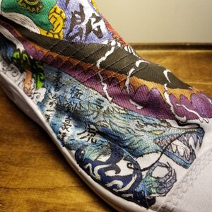 May include: A white canvas shoe with a colorful hand-painted design. The design features a blue and white dragon with sharp teeth, purple and orange waves, and Japanese characters.