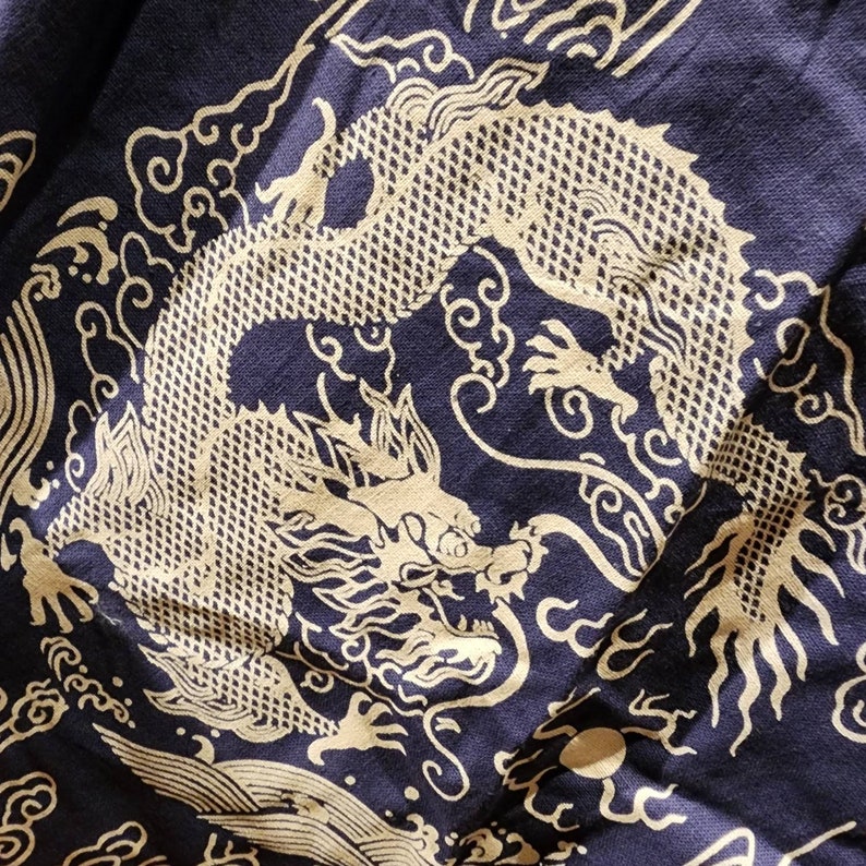 May include: A navy blue fabric with a white dragon design. The dragon is depicted in a traditional Chinese style, with swirling clouds and intricate details.