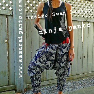 May include: A person wearing black tank top with the text "Indigo Swan Design" and white feather graphic, and blue and white patterned pants. The text "ninja pants" is visible in the background.