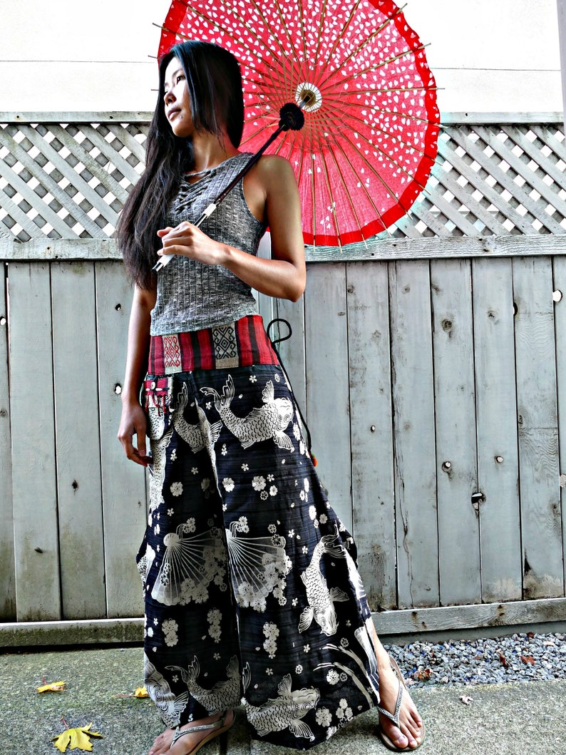 May include: A woman wearing a grey tank top and black pants with a white and black fish print. She is holding a red and white Japanese umbrella.