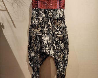 May include: Black and white patterned pants with a red and pink waistband. The pants have a loose, flowing fit and are made of a lightweight fabric.