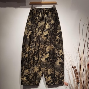 May include: Black pants with a gold floral print featuring birds and leaves. The pants have an elastic waistband and a relaxed fit.