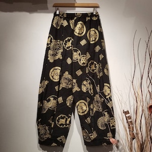 Może przedstawiać: Czarne spodnie z czarno-złotym wzorem. Wzór przedstawia tradycyjne japońskie symbole i wzory.