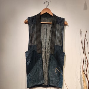Puede incluir: Un chaleco de estilo japonés tradicional de color azul y negro con parches. El chaleco está hecho de diferentes telas y tiene un diseño único.