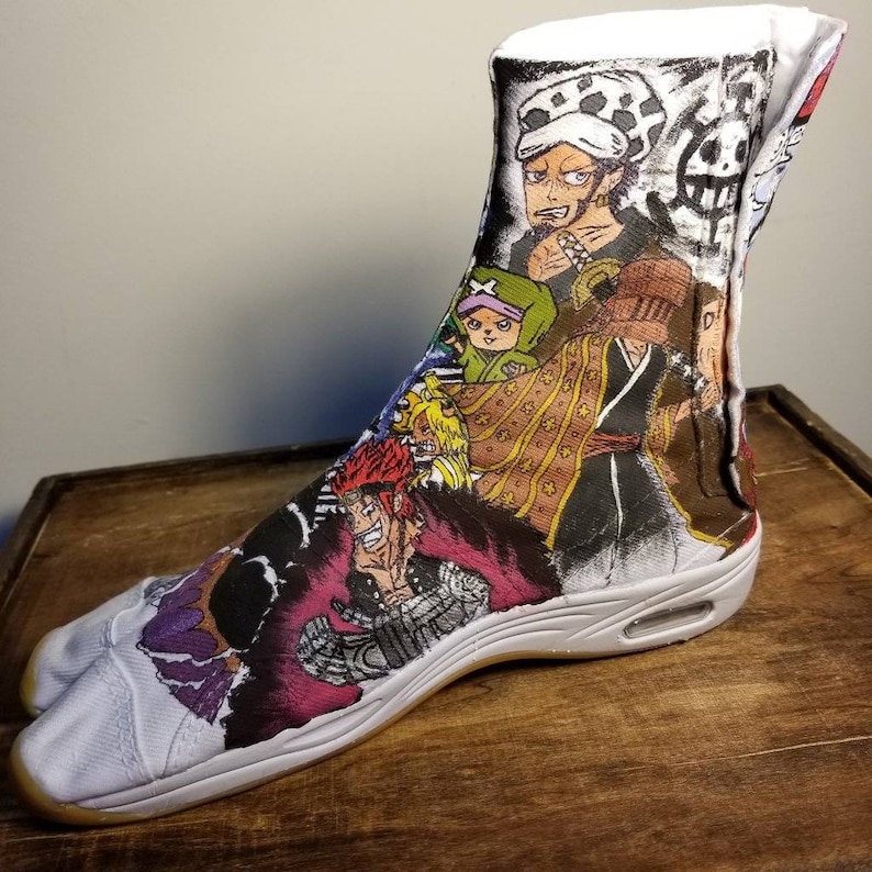 May include: White tabi shoes with a colorful anime print featuring characters from popular Japanese manga series. The print includes a character with a straw hat, a character with a green hat, and a character with red hair.