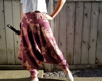 May include: Burgundy harem pants with a beige wave and mythical creature pattern. The pants have a wide, loose fit with gathered ankles. The person is wearing a gray t-shirt and striped slip-on shoes. A black katana is held in the left hand.