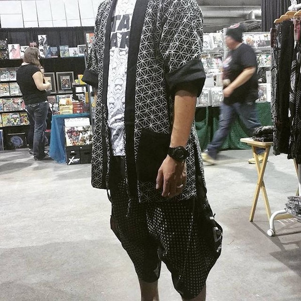 May include: A black and white geometric patterned kimono with a white t-shirt underneath. The kimono has a black collar and long sleeves. The person is wearing black and white patterned pants.