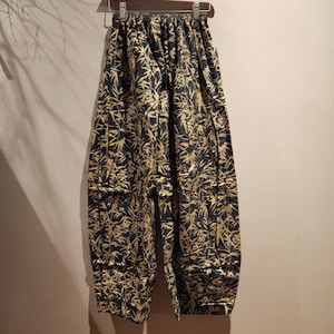 May include: Black pants with a gold bamboo print. The pants have a drawstring waist and multiple pockets.