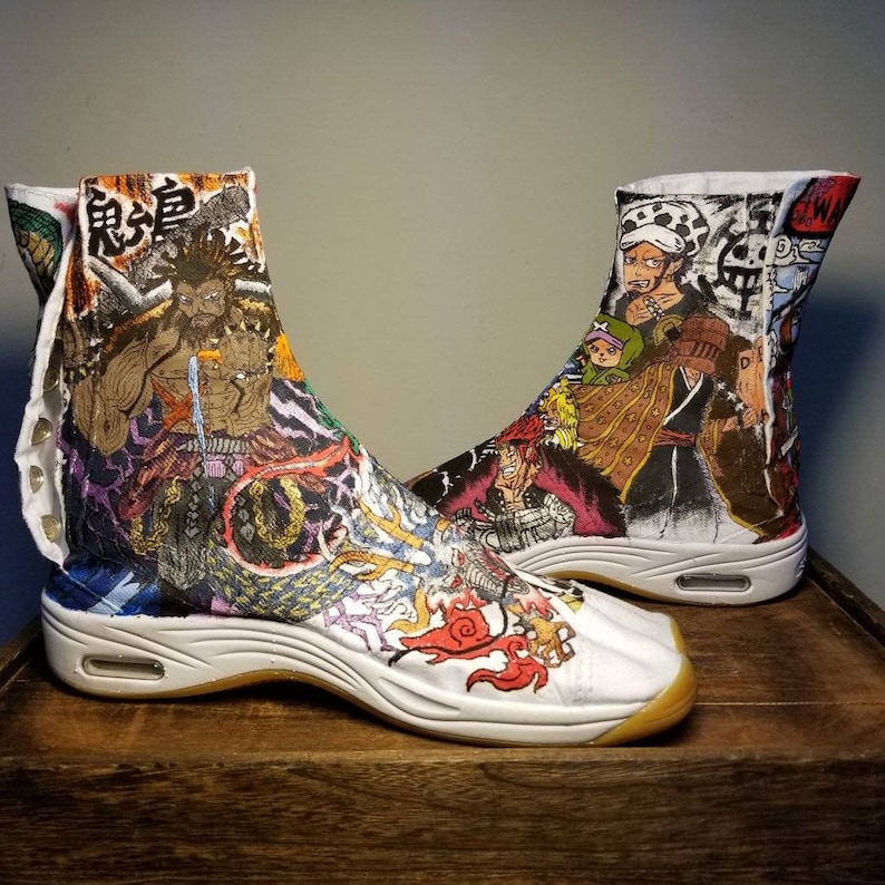 May include: A pair of white high-top shoes with a colorful anime-inspired design. The shoes feature a variety of characters, including a dragon, a samurai, and a pirate. The shoes have a thick white sole and a black rubber toe cap.