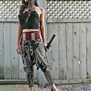 May include: A woman wearing black and white patterned pants with a red and white striped waistband. She is holding a black sword and is wearing a black tank top.