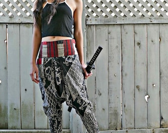 May include: A woman wearing black and white patterned pants with a red and white striped waistband. She is holding a black sword and is wearing a black tank top.