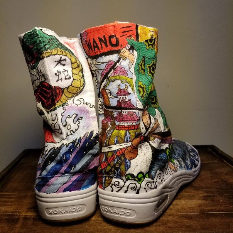 May include: A pair of white canvas high-top shoes with a colorful hand-painted design featuring Japanese characters, a dragon, and a scene from the anime One Piece. The shoes have a white sole with the word "SOKAIOD" printed on the bottom.