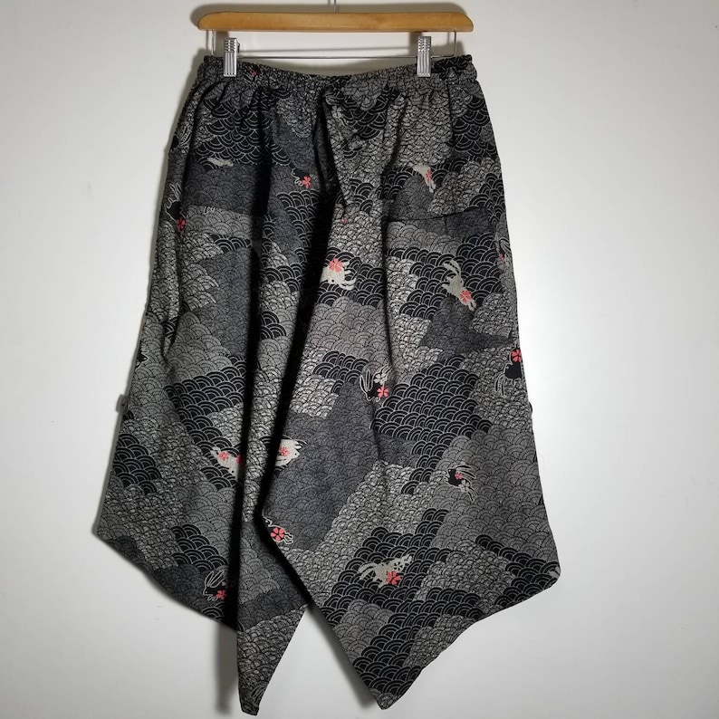 Puede incluir: Pantalones negros y grises con estampado, cintura con cord&oacute;n y corte asim&eacute;trico &uacute;nico. El estampado presenta un dise&ntilde;o repetitivo de olas y peque&ntilde;as flores rosas.