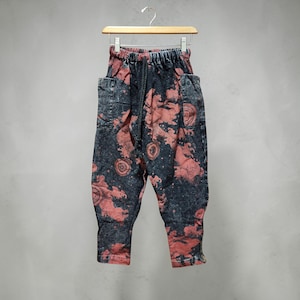 May include: Dark wash denim pants with a unique red pattern. The pants have a drawstring waist, pockets, and a relaxed fit. The fabric appears to be a medium weight denim.