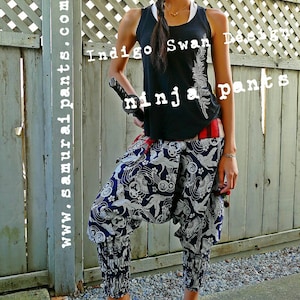 May include: A person wearing black tank top with the text "Indigo Swan Design ninja pants" and blue and white patterned pants. The pants have a loose fit and are gathered at the ankles.