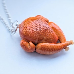 May include: A silver chain necklace with a pendant shaped like a roasted turkey. The turkey pendant is a detailed miniature with a textured, golden-brown surface, and is attached to the chain with a silver ring.