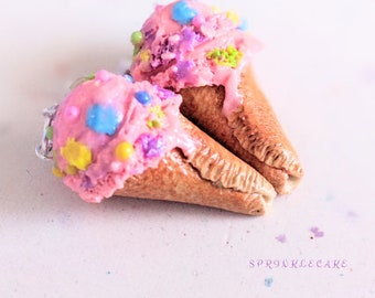 May include: Two pink ice cream cones with colourful sprinkles and a brown waffle cone. The cones are lying on a white surface with a light pink background.