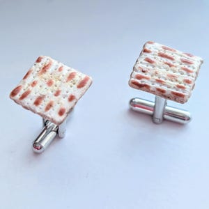 May include: A pair of silver cufflinks with a matzah design. The matzah is a traditional Jewish unleavened bread eaten during Passover.