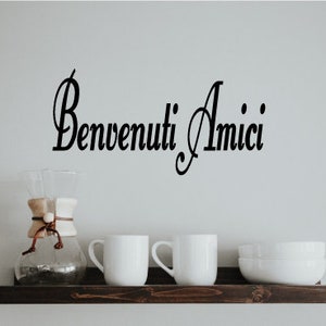 May include: A dark wooden shelf displays a glass coffee maker, two white mugs, and a stack of white bowls. The Italian phrase "Benvenuti Amici" is written in black script above the shelf.