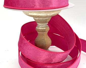 May include: A spool of pink velvet ribbon with a satin edge. The ribbon is wrapped around a wooden spool and is ready to be used for crafting or decorating.
