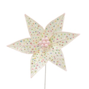 May include: A white poinsettia flower with pink glitter and colorful sprinkles. The flower has a pink center with five pink balls.