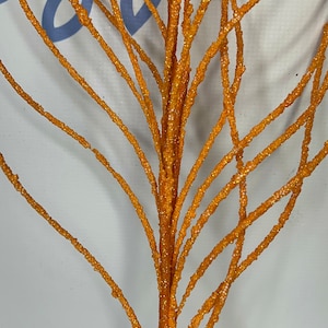 May include: Orange glittered decorative branch with multiple stems. The stems are covered in small, sparkling glitter particles. The branch is a vibrant orange color and is suitable for floral arrangements or seasonal decor.