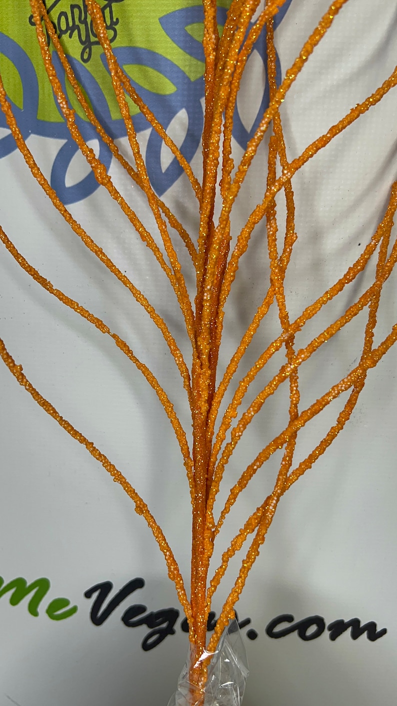 May include: Orange glittered decorative branch with multiple stems. The stems are covered in small, sparkling glitter particles. The branch is a vibrant orange color and is suitable for floral arrangements or seasonal decor.