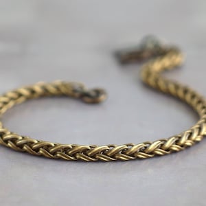 Puede incluir: Un brazalete de cadena trenzada dorada con un cierre simple.