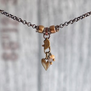 May include: A delicate gold necklace with a heart charm and small beads. The chain is made of small, linked metal rings.