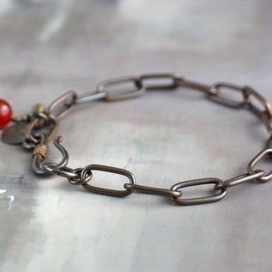May include: A silver chain bracelet with a red gemstone charm. The chain is made of oval links.