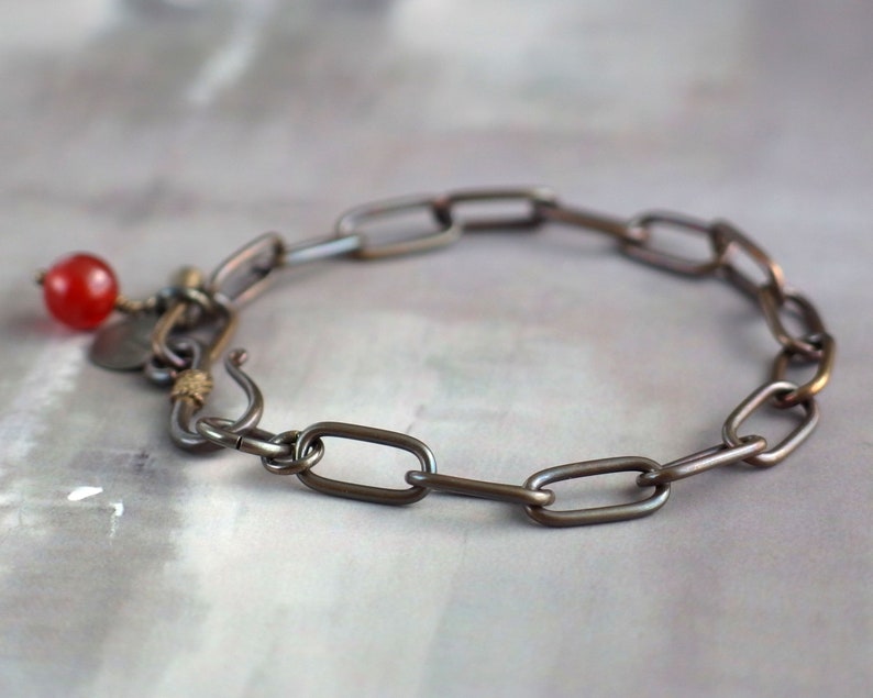 May include: A silver chain bracelet with a red gemstone charm. The chain is made of oval links.