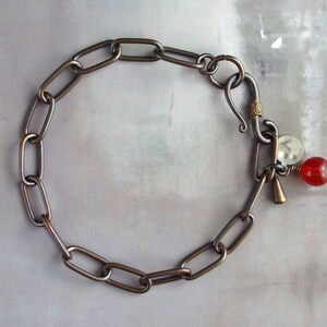May include: A silver chain bracelet with a hook clasp and a red gemstone charm.