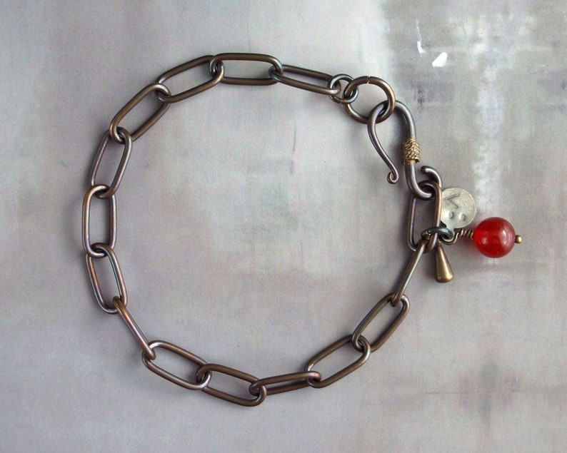 May include: A silver chain bracelet with a hook clasp and a red gemstone charm.