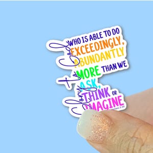 May include: A sticker with the text "Who is able to do exceedingly abundantly more than we ask or think." The text is in various colors, including yellow, green, and purple, on a white background. The sticker is held against a light blue background.