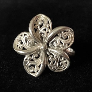 May include: A silver ring featuring a delicate, intricate floral design. The ring is crafted from filigree and shaped like a flower.