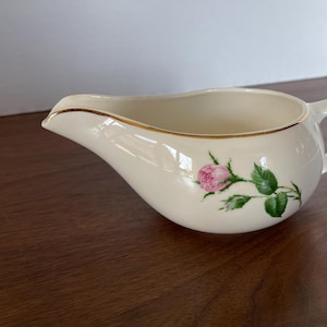 May include: A white ceramic creamer with a gold rim and a pink rose design.