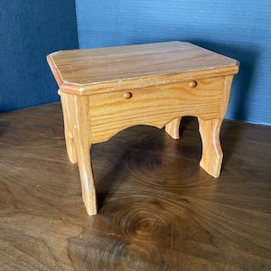 May include: A small, wooden side table with a rectangular top and two small knobs. The table has four curved legs and is made of light-colored wood. The table is approximately 18 inches long, 12 inches wide, and 16 inches tall.